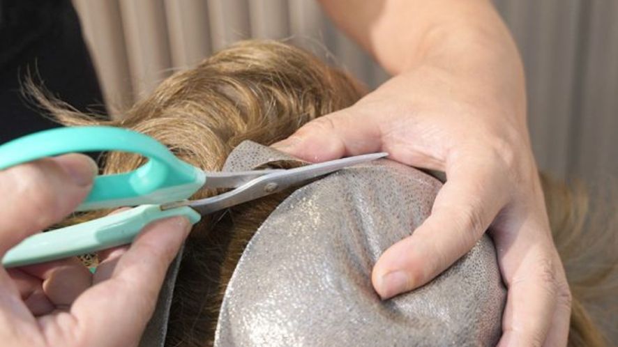 a man cutting the extra edge of a hair system