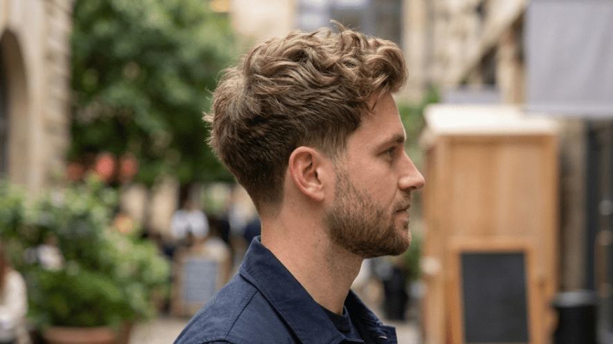 Side profile of a man with wavy, textured hair on top and a short fade on the sides.