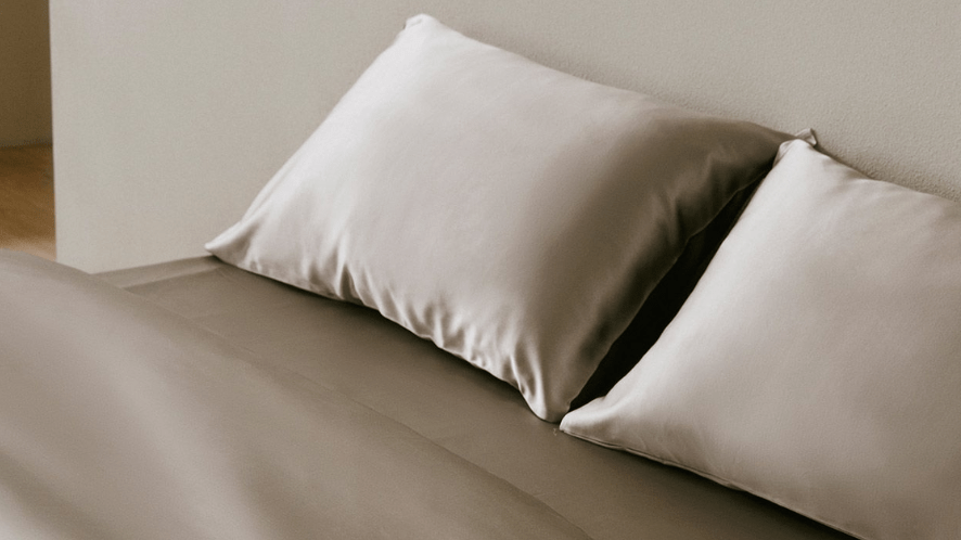 Two silk pillowcases on a bed, illustrating how smooth fabric reduces friction and prevents hair system tangling.
