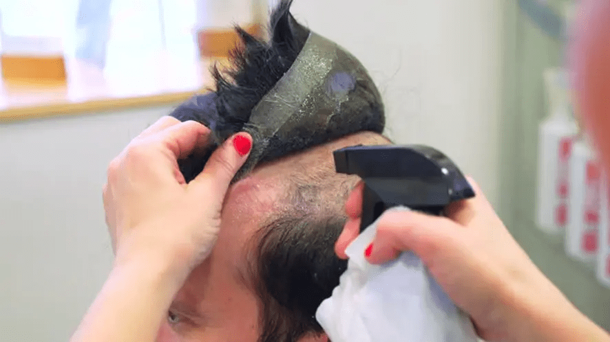 A hairstylist lifting the hair system from a customer's head