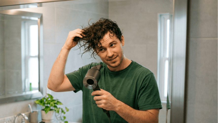 A man blowing his wet hair system using a blow dryer